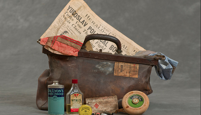 Suticase including a newspaper from the 30s with a headline of "Yugoslav political - undescipherable" and various men's toiletries.